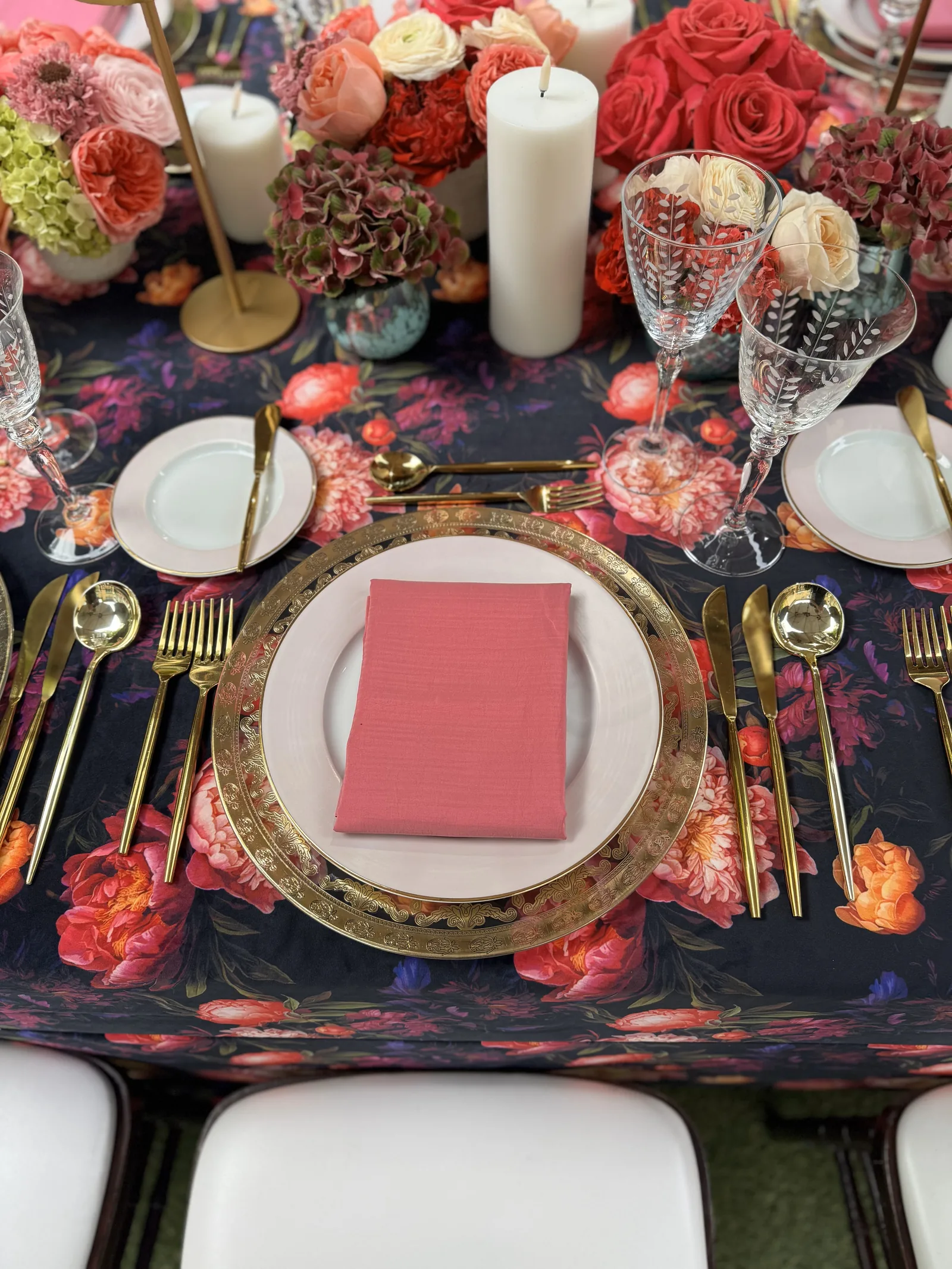 Close-up of dark floral printed table linen with a coral napkin and gold place setting